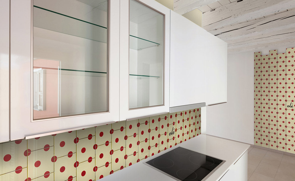 Modern kitchen with white cabinets, glass doors, and a black stovetop. The retro backsplash features Bussoga's Olé Tile Coasters with red dots on Spanish ceramic tiles. Exposed white ceiling beams add an airy touch.