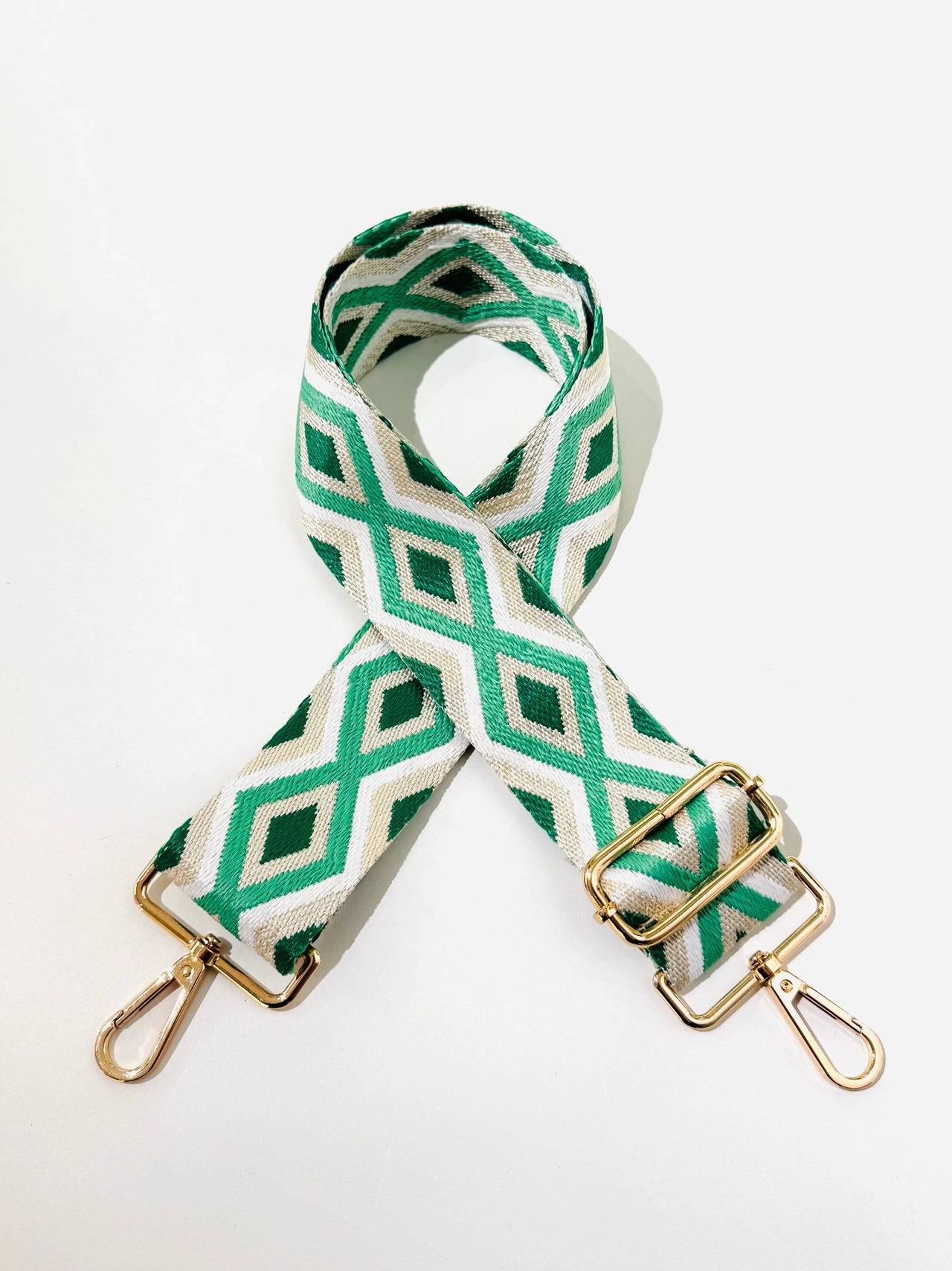 Green and white geometric patterned bag strap with gold hardware on a light gray background