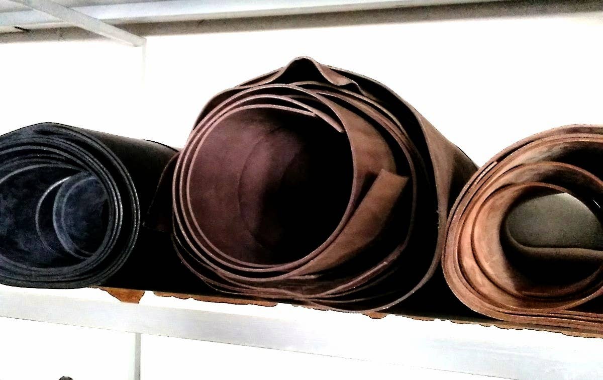 Three large rolls of black, dark brown, and light brown leather are stored on a shelf—ideal for crafting a Vaquetilla Leather Belt by Creaciones Corpas with a Zamak buckle.