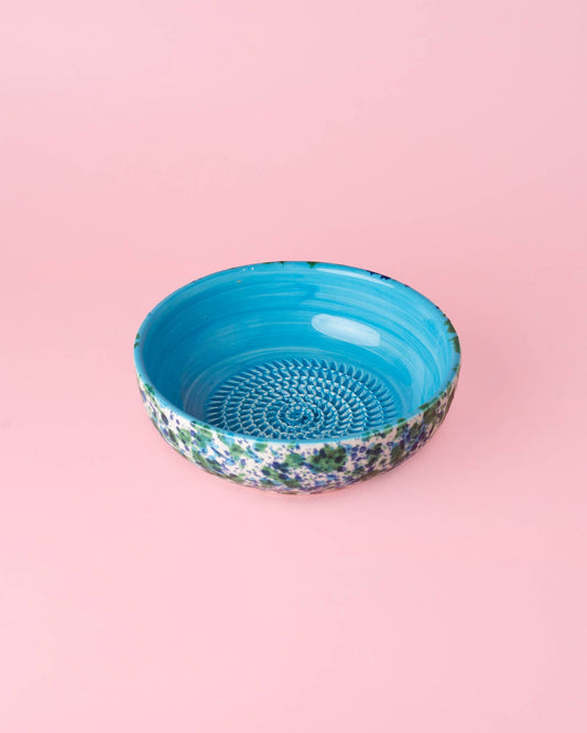 A medium ceramic Garlic Grater Plate in Azul by Alfar Tierra Cocida, featuring a floral-patterned exterior and bright blue interior, sits on a light pink background—perfect for effortless zesting and serving.