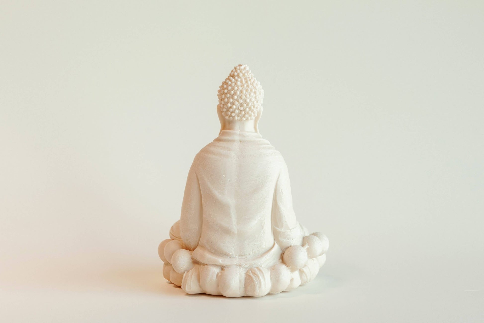 The Manulena Decorative & Aromatic Buddha Piece (White) shows a Buddha seated cross-legged on a lotus pedestal, viewed from behind, set against a plain, light background.