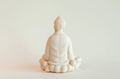 The Manulena Decorative & Aromatic Buddha Piece (White) shows a Buddha seated cross-legged on a lotus pedestal, viewed from behind, set against a plain, light background.