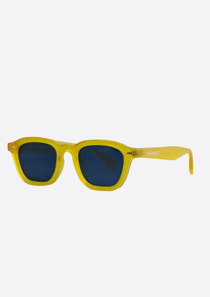 Oceanides Neda Yellow Frosted Sunglasses feature thick yellow recycled plastic frames and rounded rectangular blue lenses, shown against a plain white background.
