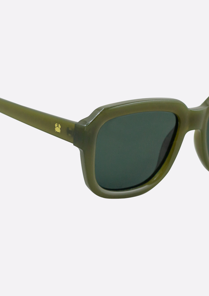 Close-up of Oceanides Petrea Low Verde Sunglasses in green recycled plastic with dark lenses. A gold bee emblem accents the left arm near the hinge, set against a plain white background.