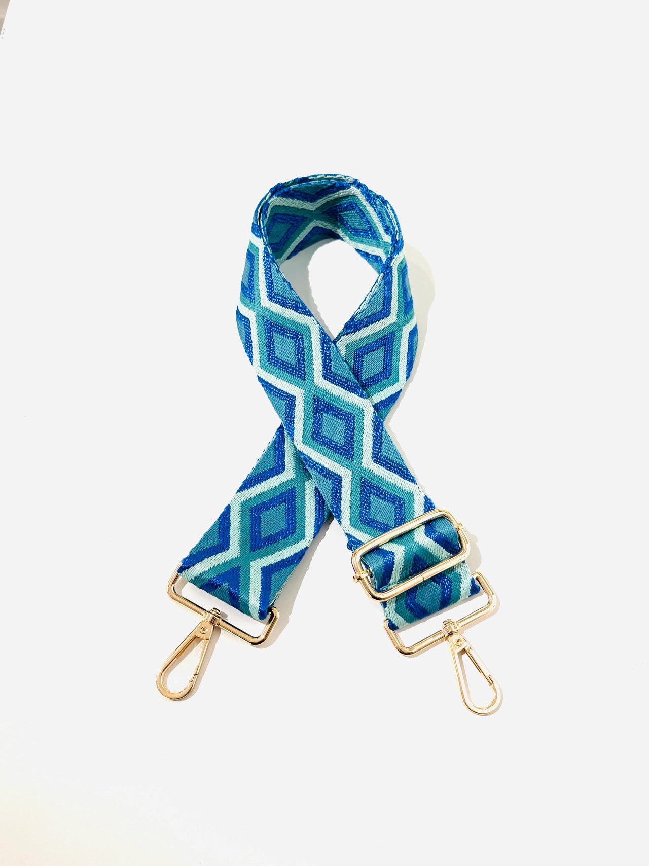 Blue geometric patterned bag strap with gold hardware on a white background