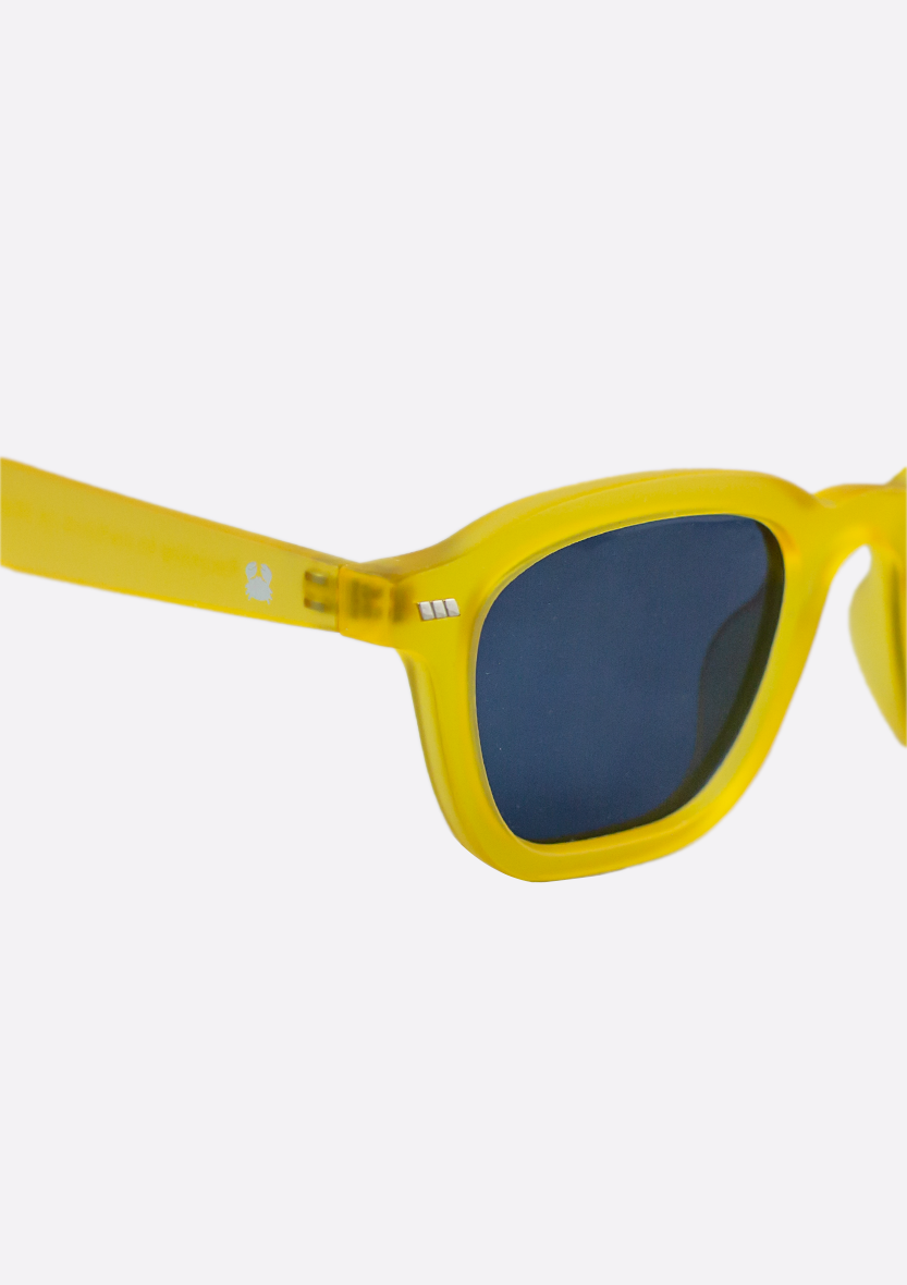 Close-up of Oceanides Neda Yellow Frosted Sunglasses with dark lenses, featuring part of the left frame and arm against a white background—crafted from recycled plastic for eco-friendly style.