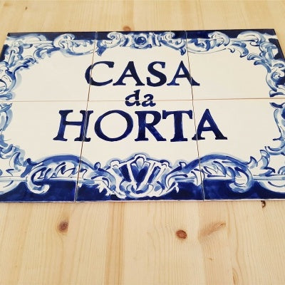 TilePassion’s Bespoke Outdoor House Address Portuguese Tile Mural in Cobalt Blue features ornate blue borders and “Casa da Horta” hand-painted on ceramic, evoking classic Portuguese style, presented on a light wooden surface.