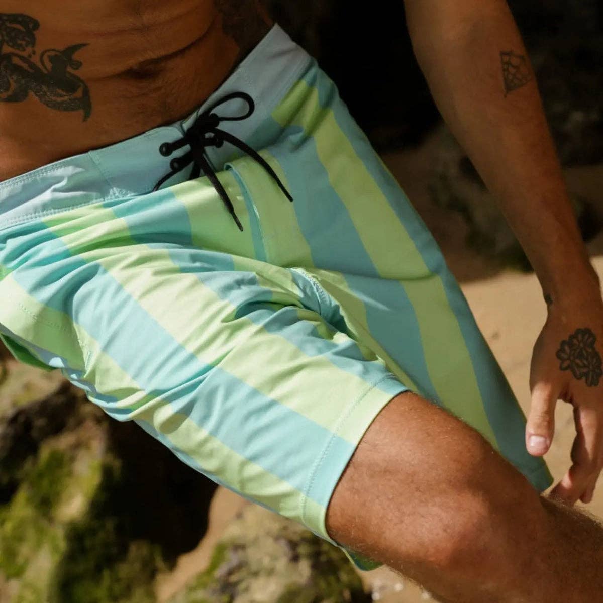 Man wearing Futah x 38graus blue and green striped boardshorts by the beach