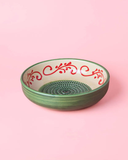 The Alhambra Grater Bowl - Large by Alfar Tierra Cocida is a green ceramic bowl featuring an Alhambra-inspired inner rim design, beautifully handcrafted in Spain and shown on a pink background.