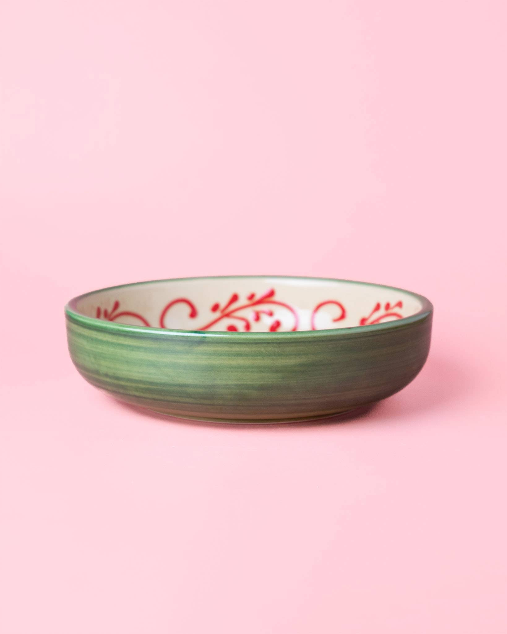 The Alhambra Grater Bowl - Large by Alfar Tierra Cocida is a green ceramic bowl with a white interior featuring red swirls, inspired by handcrafted Spanish kitchenware and shown on a light pink background.