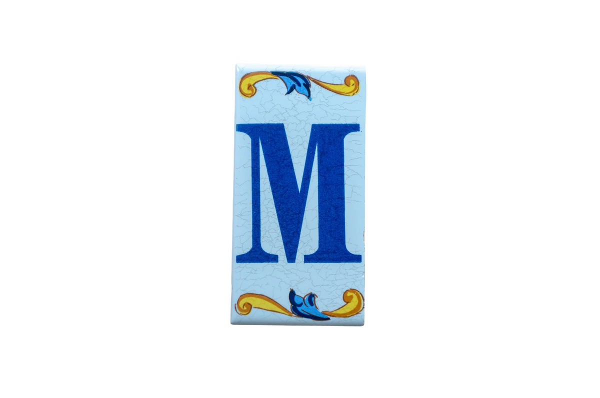 Lisa Croquets Letters – Ceramic House Letter Tile featuring a rectangular Spanish design with a blue letter M and decorative yellow and blue scrolling flourishes at the top and bottom.