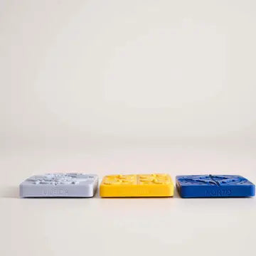 The Manulena Portuguese Azulejo Scented Magnet Set features three square magnets—light gray, yellow, and dark blue—inspired by Portuguese tiles with textured designs, arranged in a row on a plain surface.