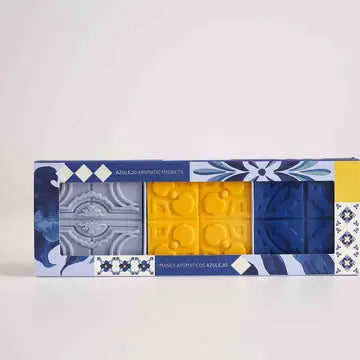 The Manulena Portuguese Azulejo Scented Magnet Set features three decorative tile-shaped magnets in gray, yellow, and blue, beautifully packaged with floral and geometric designs inspired by Portuguese tile decor.