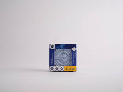 The Manulena Sintra Aromatic Tile Magnet, inspired by Portugal’s enchanted hills, is a small blue and white ceramic magnet with a decorative pattern. The packaging displays LISBOA in yellow—a charming Portuguese souvenir.