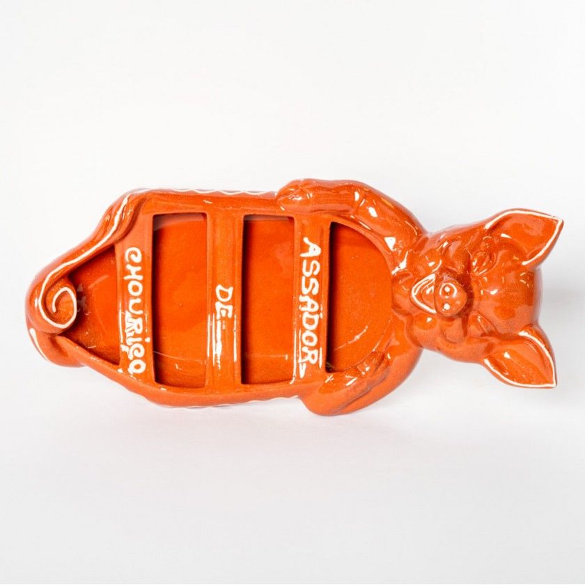 The Terracotta Chorizo Pig Roaster by Ceramica Picas is an orange-glazed ceramic tray with three slots and "Chouriço de Assar" in white—perfect for flaming and serving Portuguese chorizo.