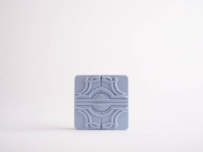 The Sintra Aromatic Tile Magnet by Manulena, inspired by Portugal’s enchanted hills, features a light blue rectangular ceramic design with an ornate symmetrical embossed pattern, displayed on a plain white background.