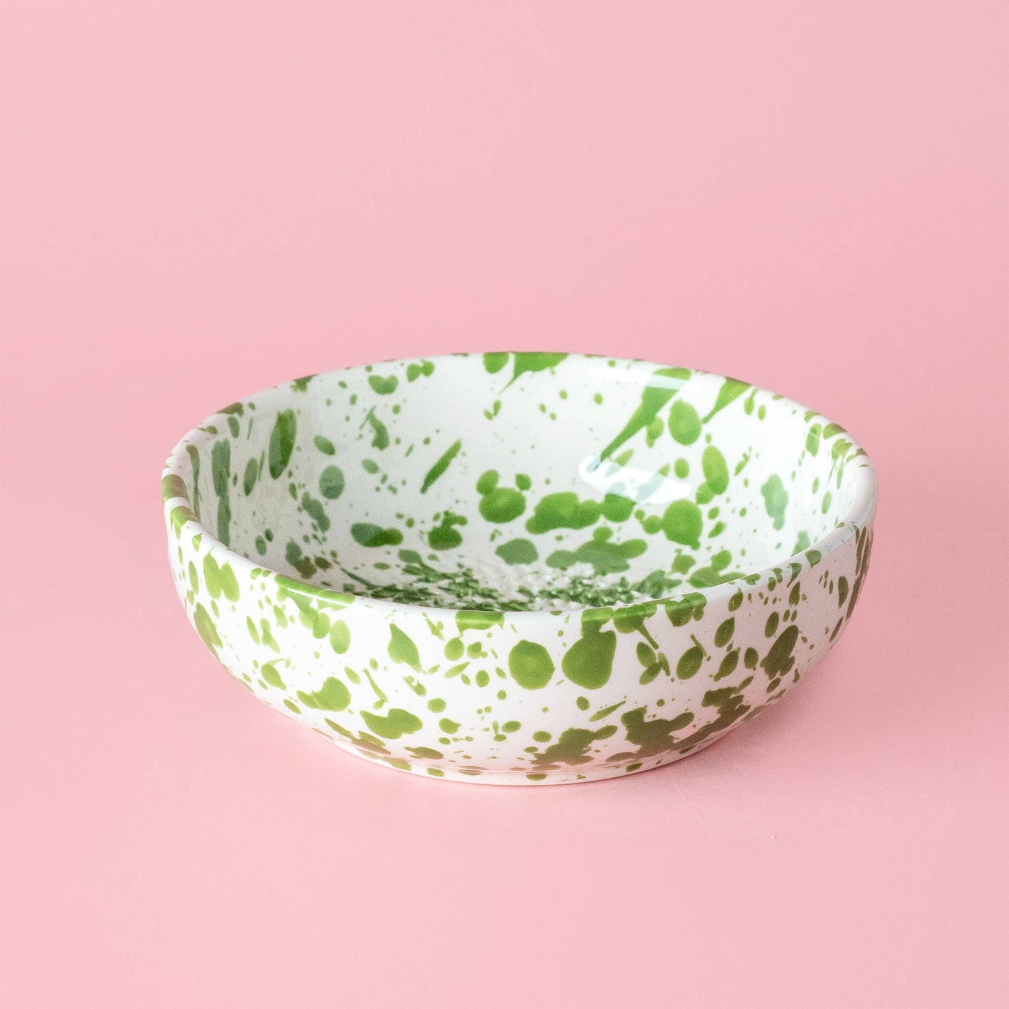 The Garlic Grater Plate - Medium Ceramic Green - Moss by Alfar Tierra Cocida is a handmade Spanish ceramic bowl with green splatters on white, shown on a light pink surface.