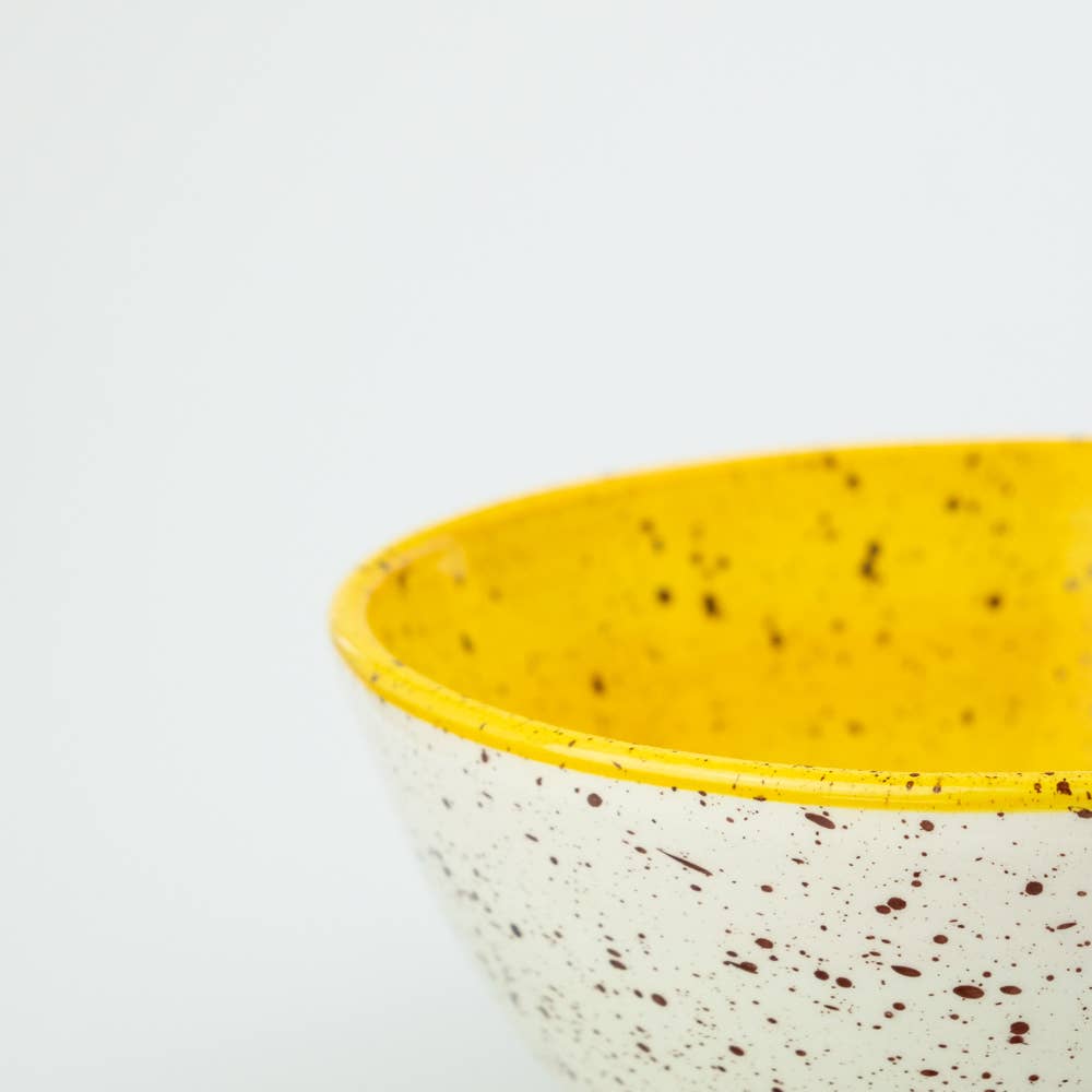Side view of a ceramic white and yellow bowl with black flecks